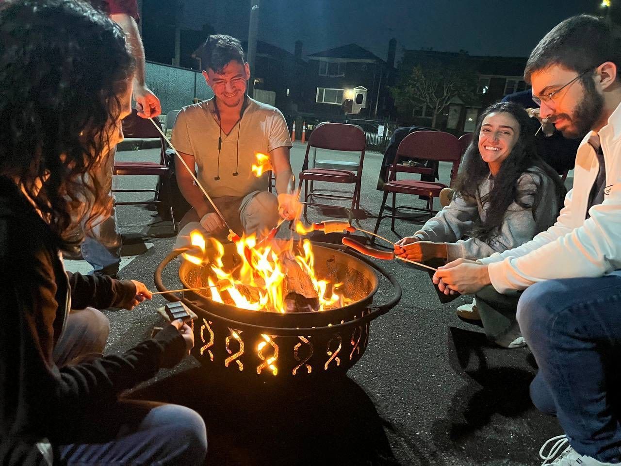 People sitting around a fire pit at night, smiling and roasting marshmallows outdoors.