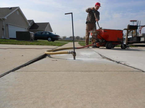 Residential Services — Home Outdoor Flooring in Lincoln, IL Close-up of a contractor performing concrete raising on a sidewalk, mud jacking a drilled hole.