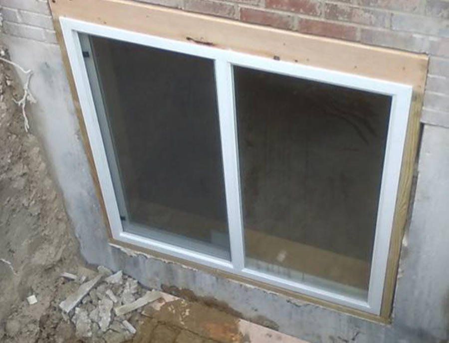 A window is being installed in the basement of a brick house | Jack-A-Slab Construction