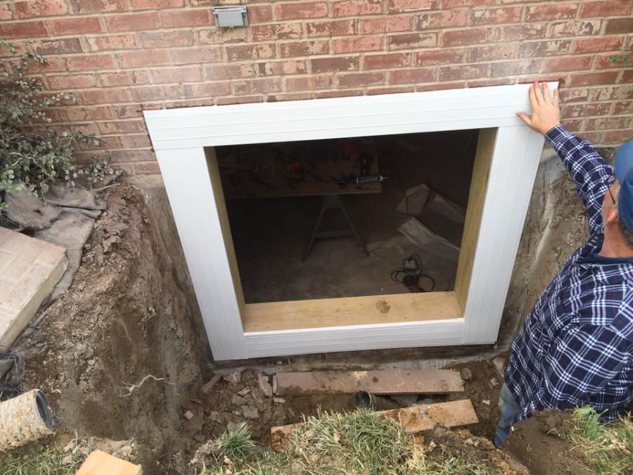 A man is working on a Egress window in a basement.
