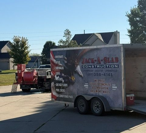 Utility trailer with Jack-A-Slab Construction branding parked in a suburban driveway beside a red machine Utility trailer with Jack-A-Slab Construction branding parked in a suburban driveway beside a red machine