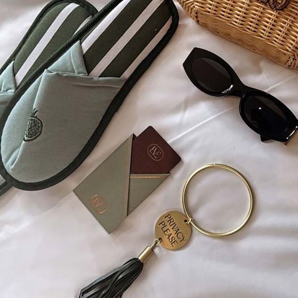 Mint slippers, black sunglasses, gold keychain, and folded cards on a white bedspread.