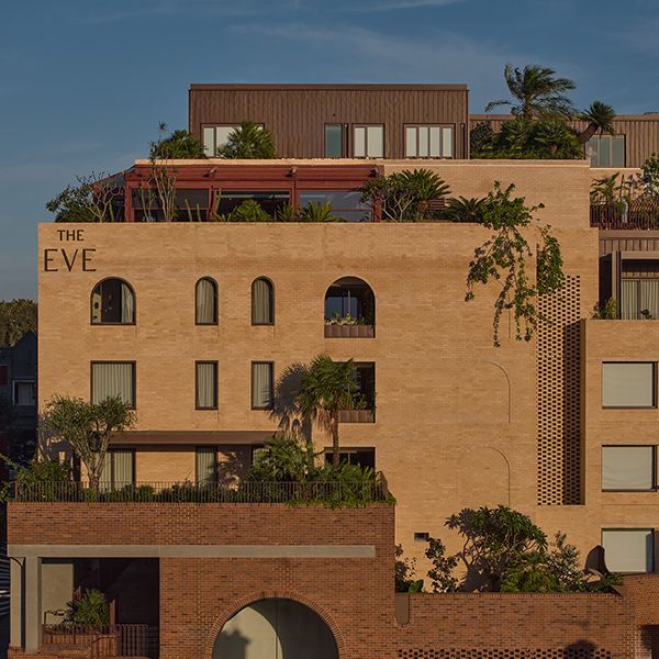 Sunlit tan and terracotta EVE Hotel with arched windows and rooftop greenery at dusk