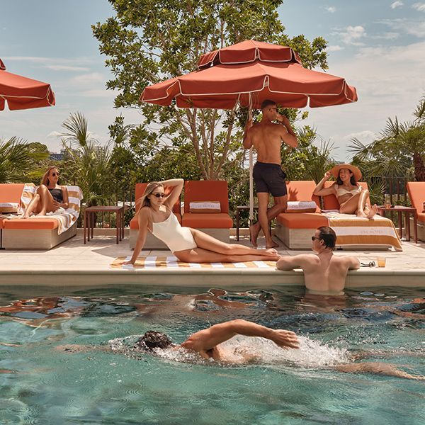 Lifestyle scene with people relaxing under red umbrellas and swimming in The EVE's rooftop pool.