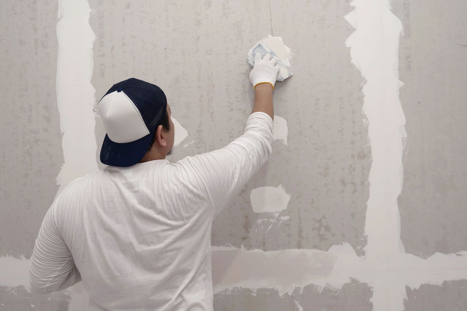 Person in white shirt and cap painting a wall with a roller during home renovation.