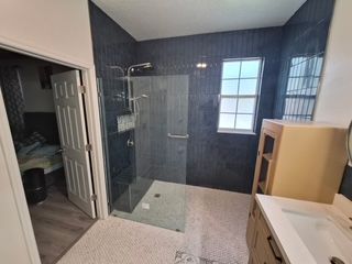 Modern bathroom with glass shower, dark tile walls, white vanity, and window natural light