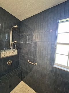 Dark-tiled bathroom with walk-in shower, wall-mounted controls, and a frosted window.