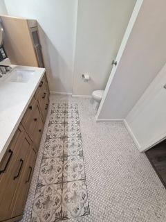 Narrow kitchen hallway with patterned tile runner, wood cabinets, and light carpeted floor by a doorway