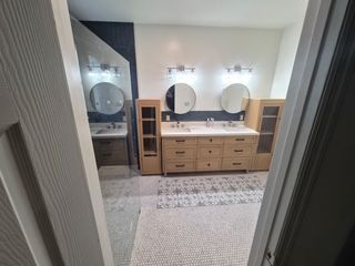 Bathroom vanity with double sinks, round mirrors, and wood cabinets seen through a doorway
