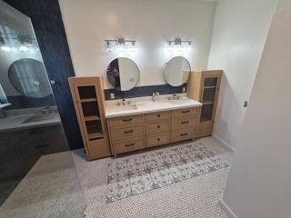Double vanity bathroom with wood cabinets, two round mirrors, and a patterned rug on the floor