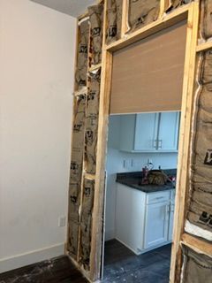 Partially renovated doorway with exposed framing and insulation, opening into a white kitchen with cabinets and sink