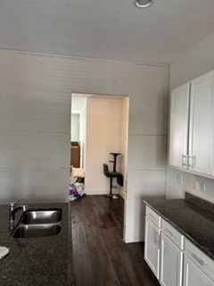 Small kitchen with white cabinets, dark countertops, a double sink, and a doorway to a hallway beyond.
