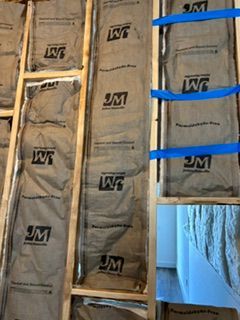 Insulated wall studs with gray batts and blue strapping, viewed from inside an unfinished room