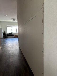 Narrow hallway with dark wood floors leading to a bright room with windows at the end