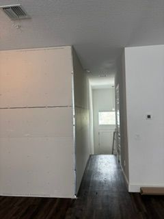 Narrow hallway with white walls and dark wood floor leading to a bright window in the distance