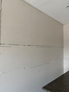 White drywall with seams and screw marks in an unfinished interior corner beside a dark countertop.