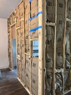 Insulated interior wall framing with exposed studs, blue tape, and a window opening under construction