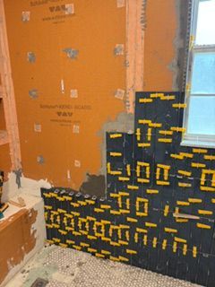 Bathroom wall under renovation with orange waterproofing and black/yellow tile work near a window.