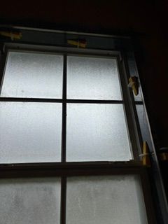 Frosted window with dark frame and a latch, seen from indoors in dim light