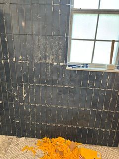 Damaged black-tiled wall with a window and orange debris piled on the floor
