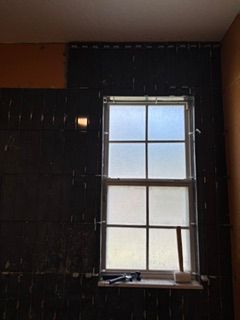 Dim room with a single window and dark unfinished walls, light coming through the panes.