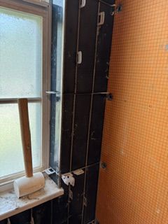 Bathroom window beside a dark shower wall and tiled orange wall, with a frosted pane and ledge.