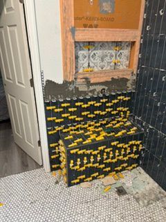Partially tiled bathroom wall with exposed plaster and stacked black-and-yellow materials beside a door