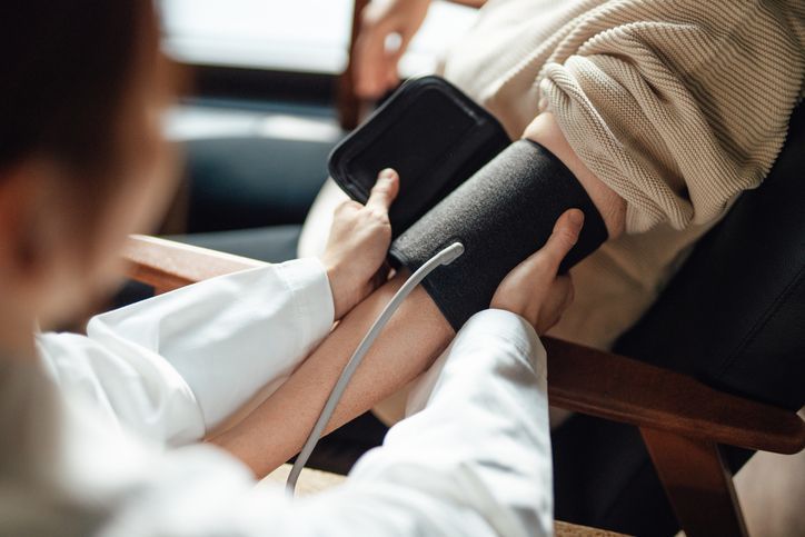 Woman has blood pressure checked by another woman, at a table.