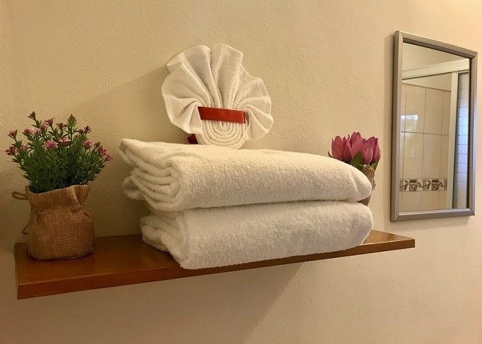 A shelf with a stack of towels and a vase of flowers on it.