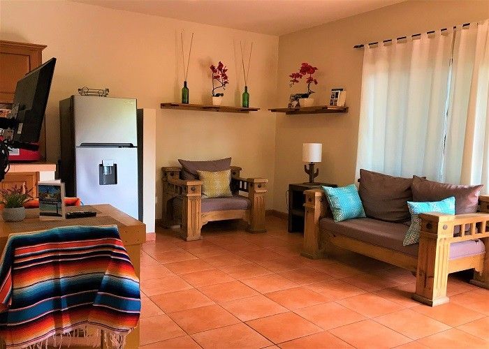 A living room with a couch , chair , table and refrigerator.