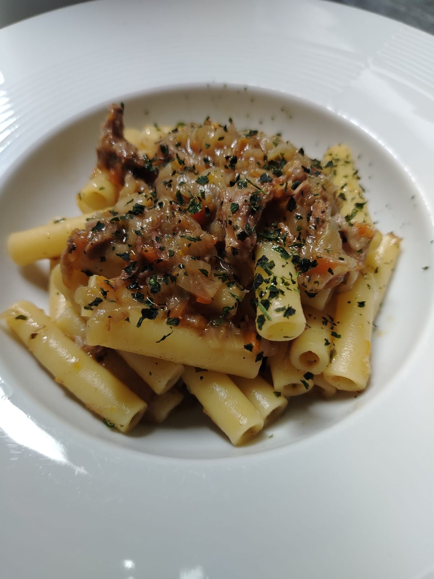 Piatto di pasta con sugo di carne in una ciotola bianca, guarnito con prezzemolo.