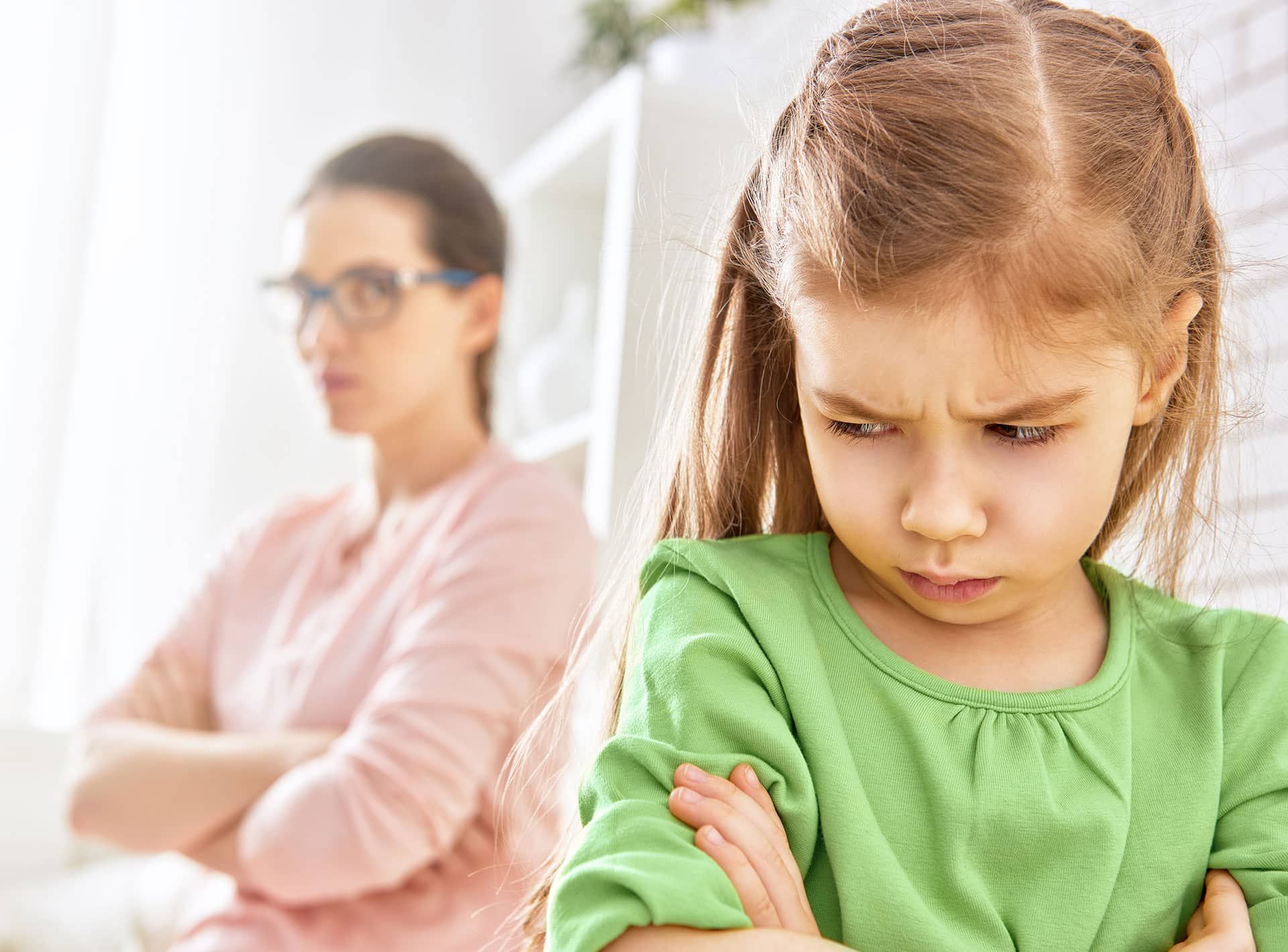 A little girl is standing in front of a woman with her arms crossed.