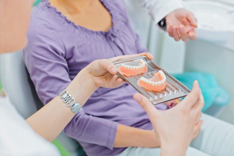 Woman in dentist chair being shown dentures on a tray by a dental professional.