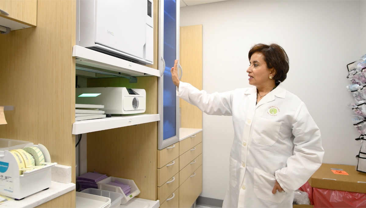 A person in a lab coat opens a cabinet holding medical equipment in a clinic setting.