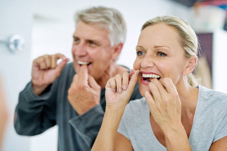 Couple flossing teeth in bathroom, smiling.