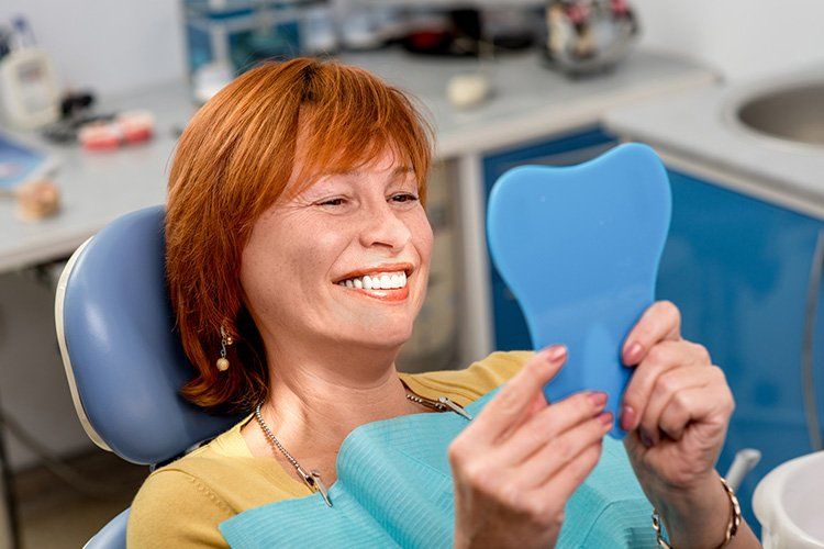 Woman with red hair smiles at her reflection in a dental mirror in a dentist's office.