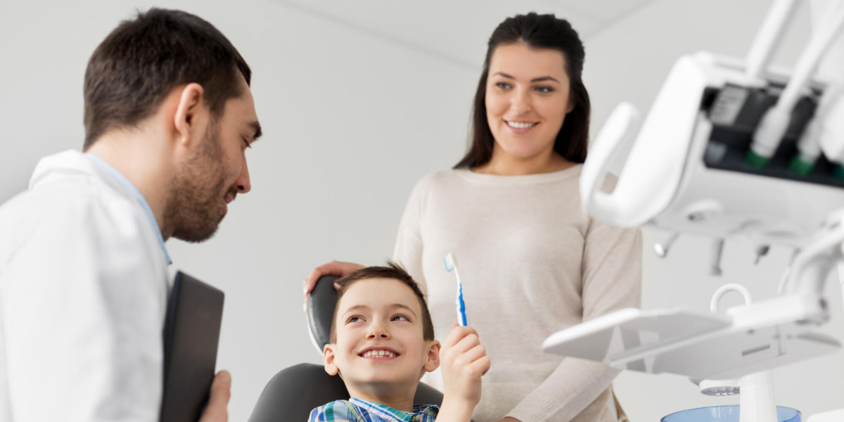 Dentist and assistant with smiling child holding toothbrush in a dental clinic