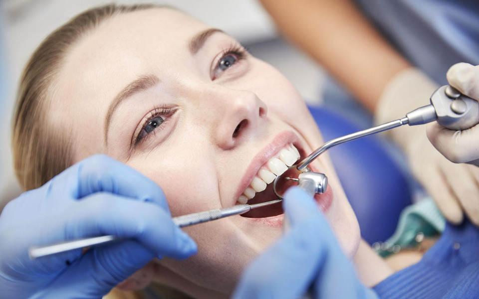 Dentist examining a smiling patient’s teeth with dental tools and blue gloves