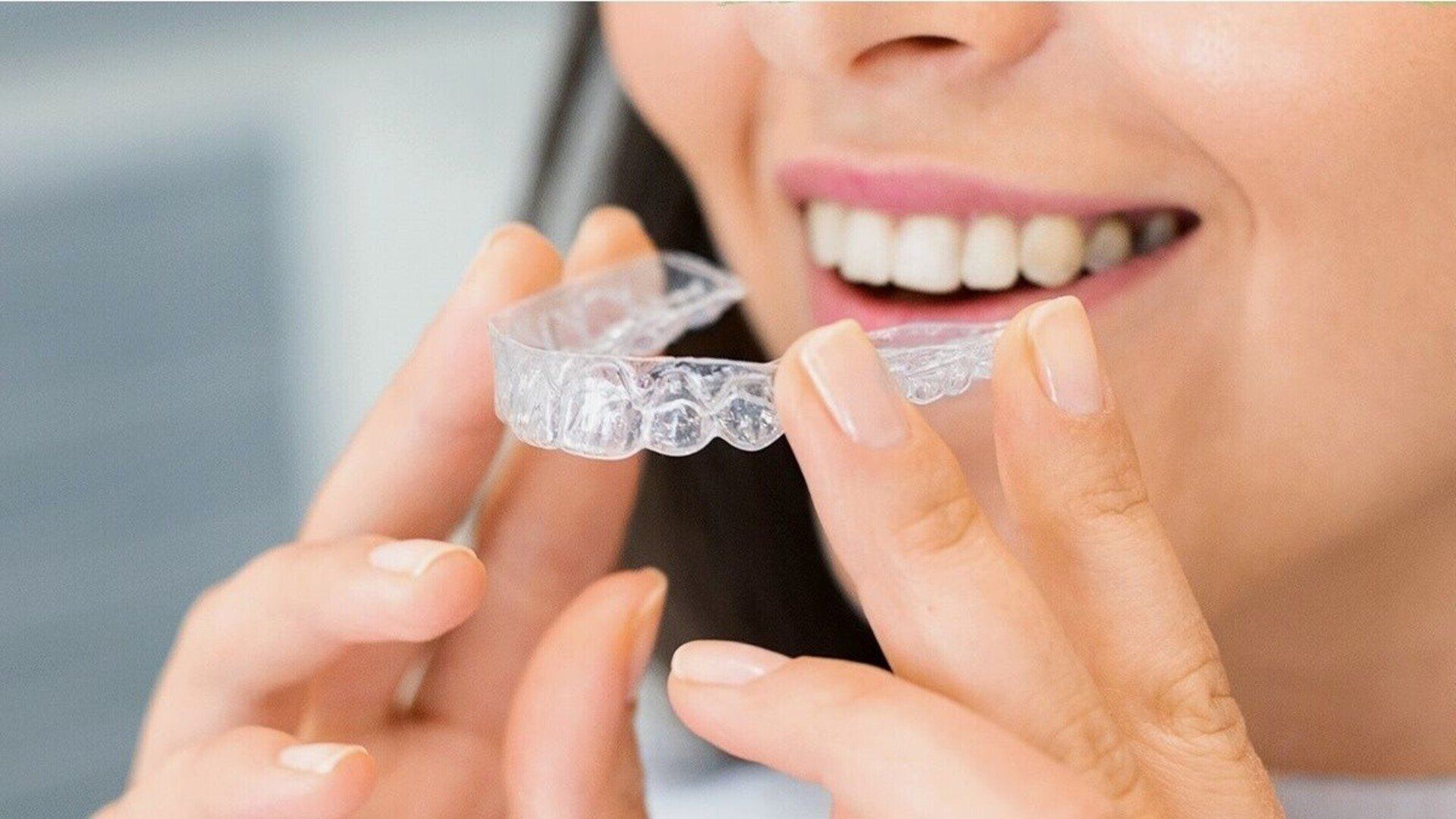 Woman holding clear aligner, smiling, ready to insert it into mouth.