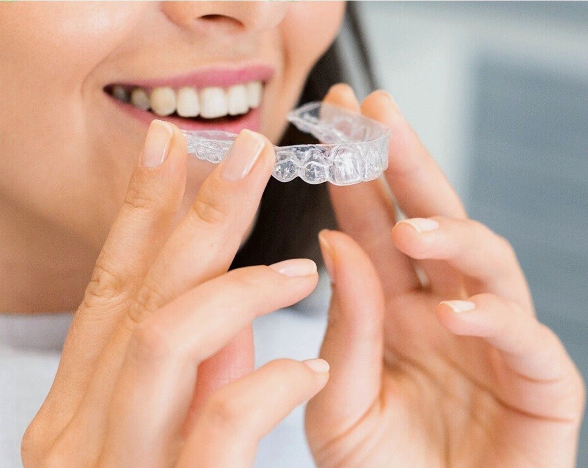 Woman smiling, holding clear aligner tray near teeth.
