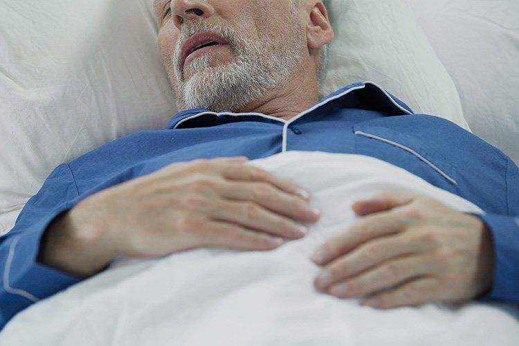 Elderly man sleeping in bed, wearing blue pajamas, white bedding.