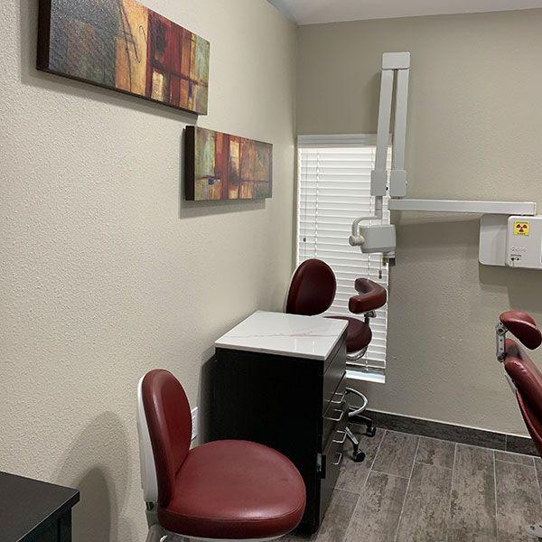 A dental office with two chairs, a table, and an x-ray machine.