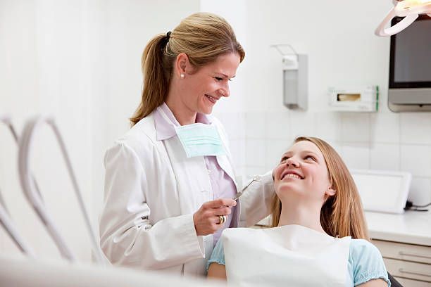 A woman is sitting in a dental chair talking to a dentist.