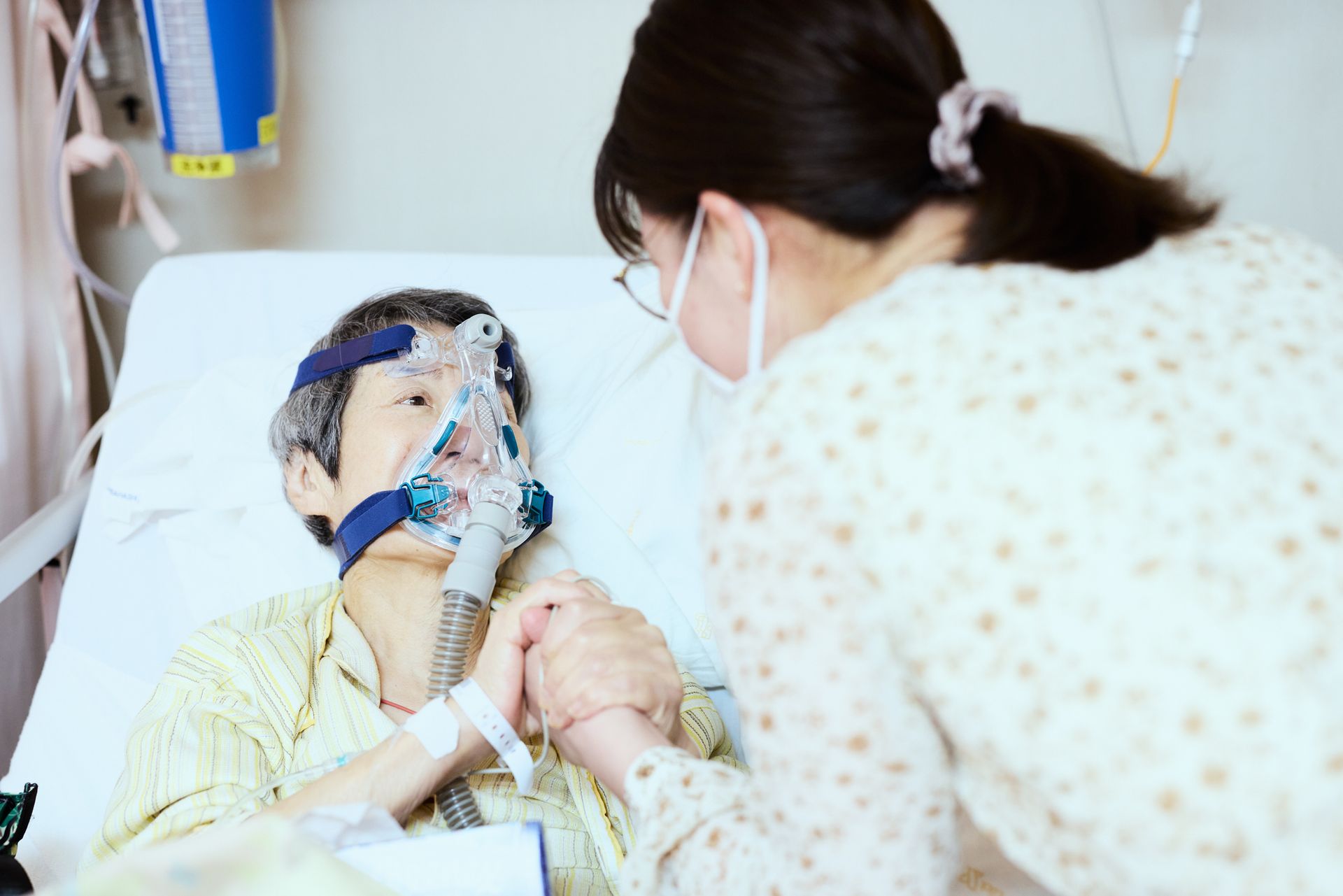 A woman is holding the hand of an elderly woman in a hospital bed. A woman is holding the hand of an elderly woman in a hospital bed.