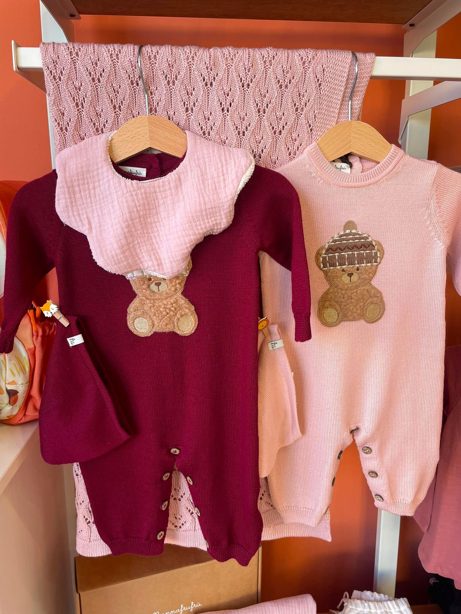 Due completi in maglia per neonati appesi a una gruccia, uno bordeaux e uno rosa con disegni di orsacchiotti.