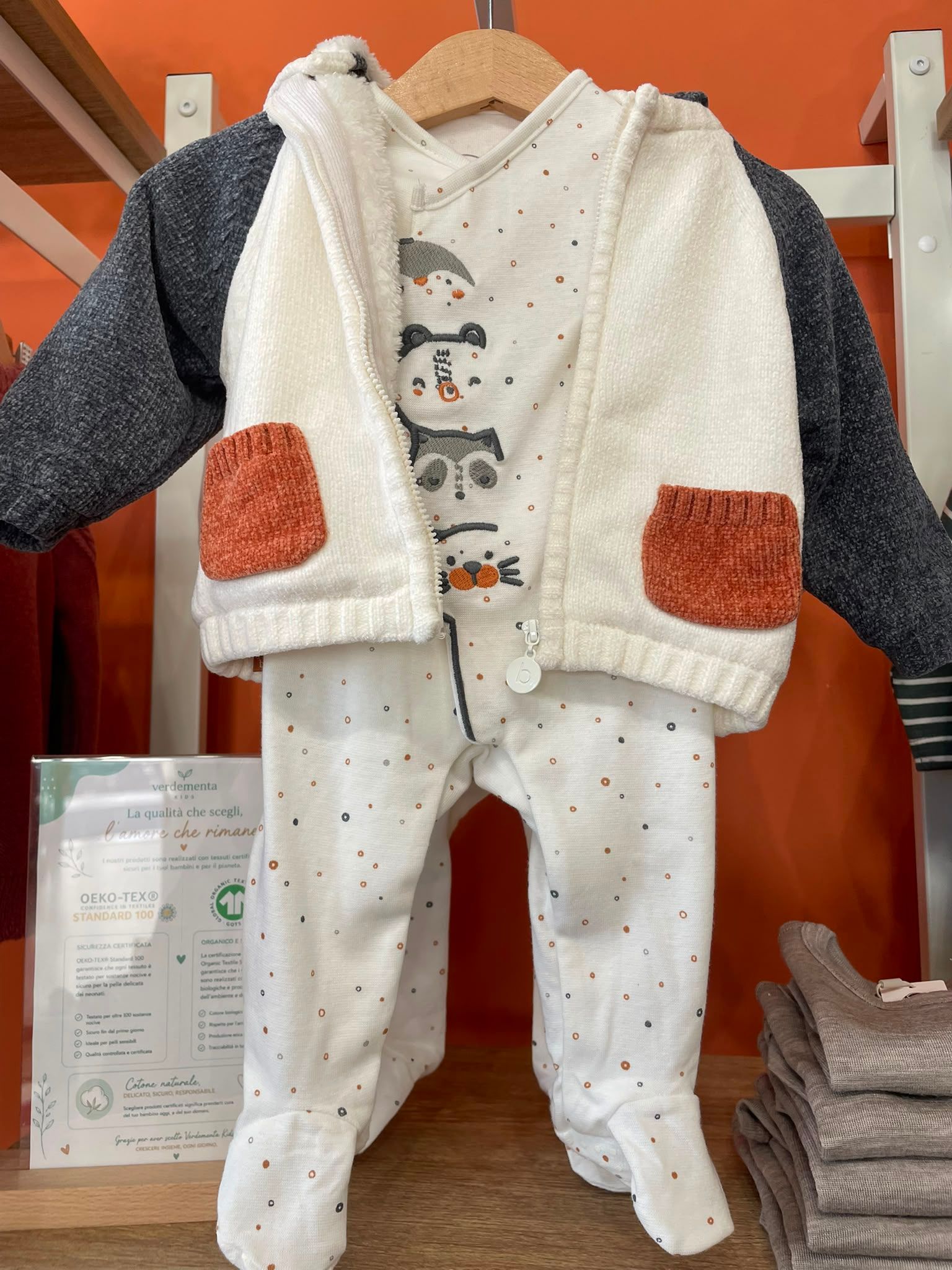 Completo bianco per neonato con gilet a stampa di pupazzo di neve e tasche applicate arancioni, appeso a un espositore