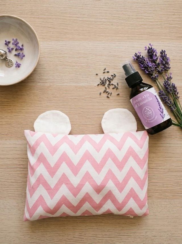 Bustina rosa con motivo a zigzag, fazzoletti bianchi, fiori di lavanda e una boccetta su un tavolo di legno