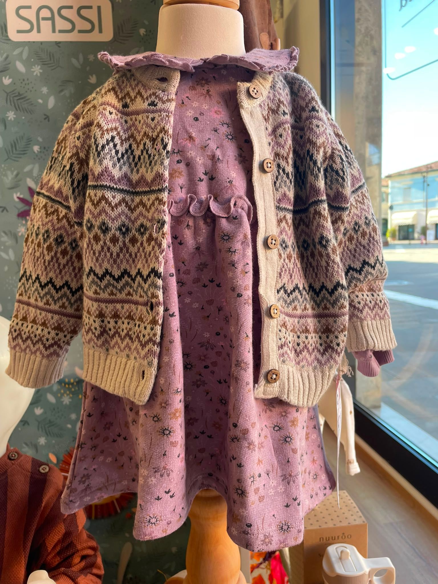 Abito floreale rosa con cardigan in maglia color crema e marrone esposto su un manichino in vetrina.