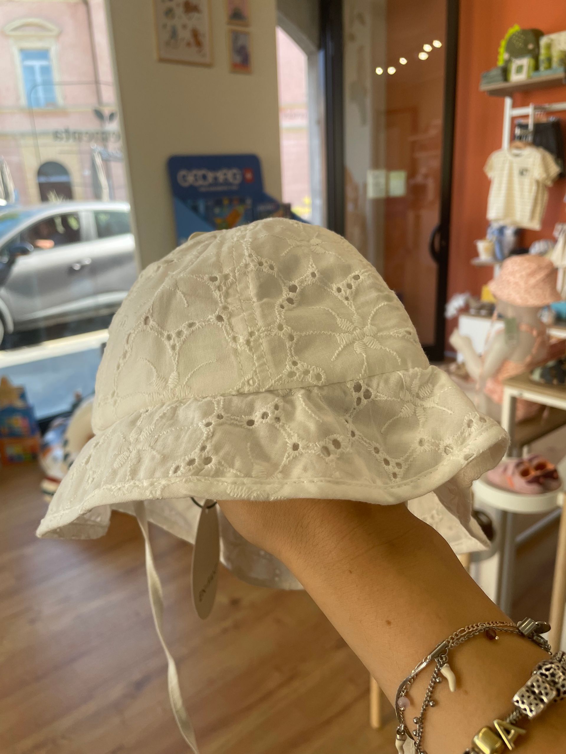 Una mano tiene in mano una cuffietta bianca di pizzo in una vetrina di negozio