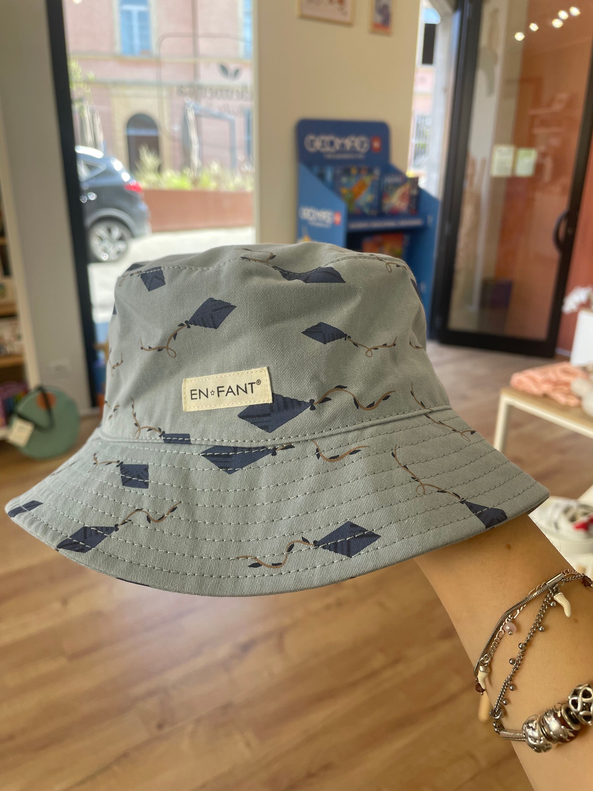 Cappello a secchiello grigio fantasia, tenuto al chiuso, con una piccola etichetta bianca sul davanti.